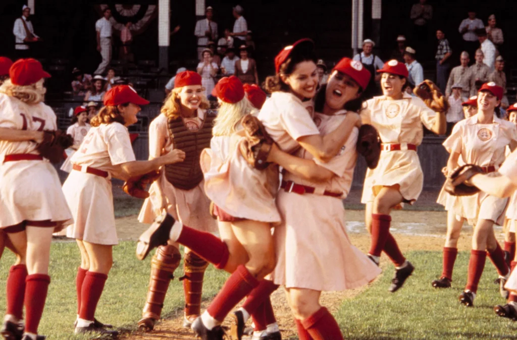 image from the movie "A League of Their Own" showing several female baseball players embracing in celebration on a baseball field after a victory